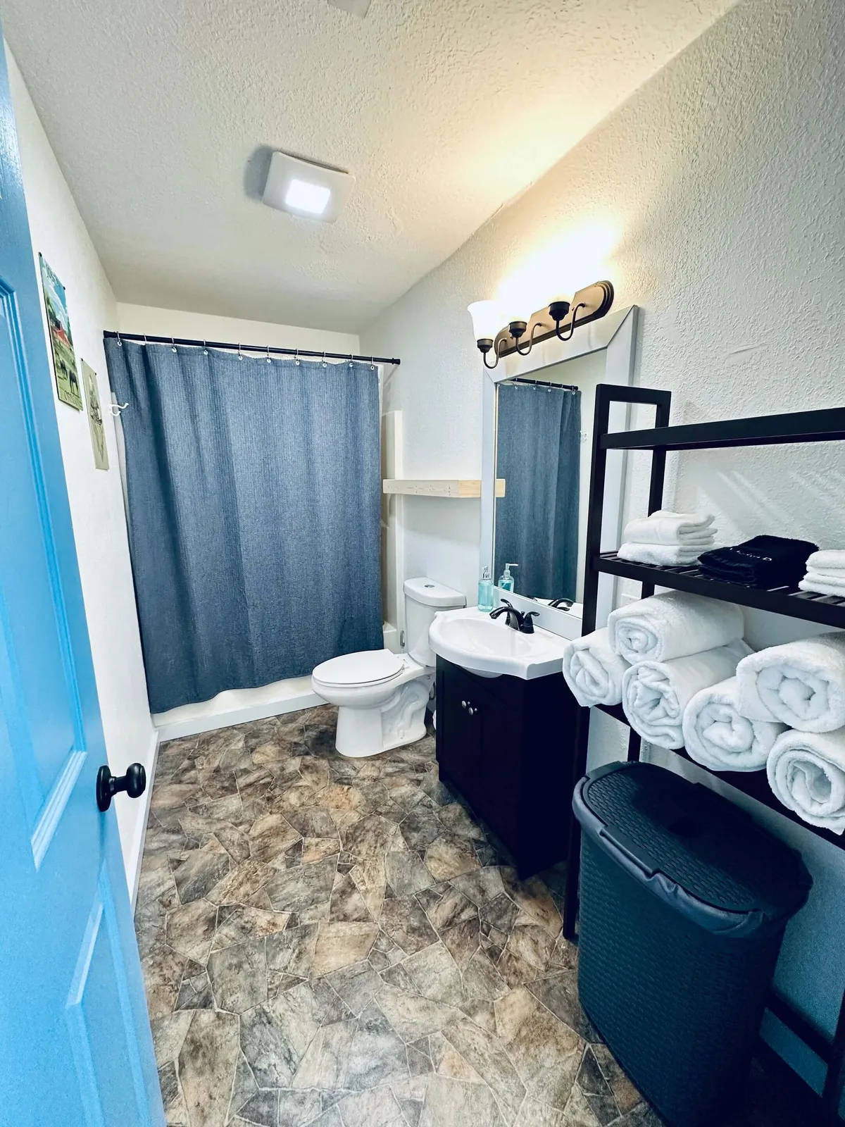 This image displays a modern bathroom with a blue door, a shower curtain, and a clean vanity with sink. The space feels inviting, practical, and well-maintained—suggesting fresh towels, ample hot water, and a pleasant self-care environment.