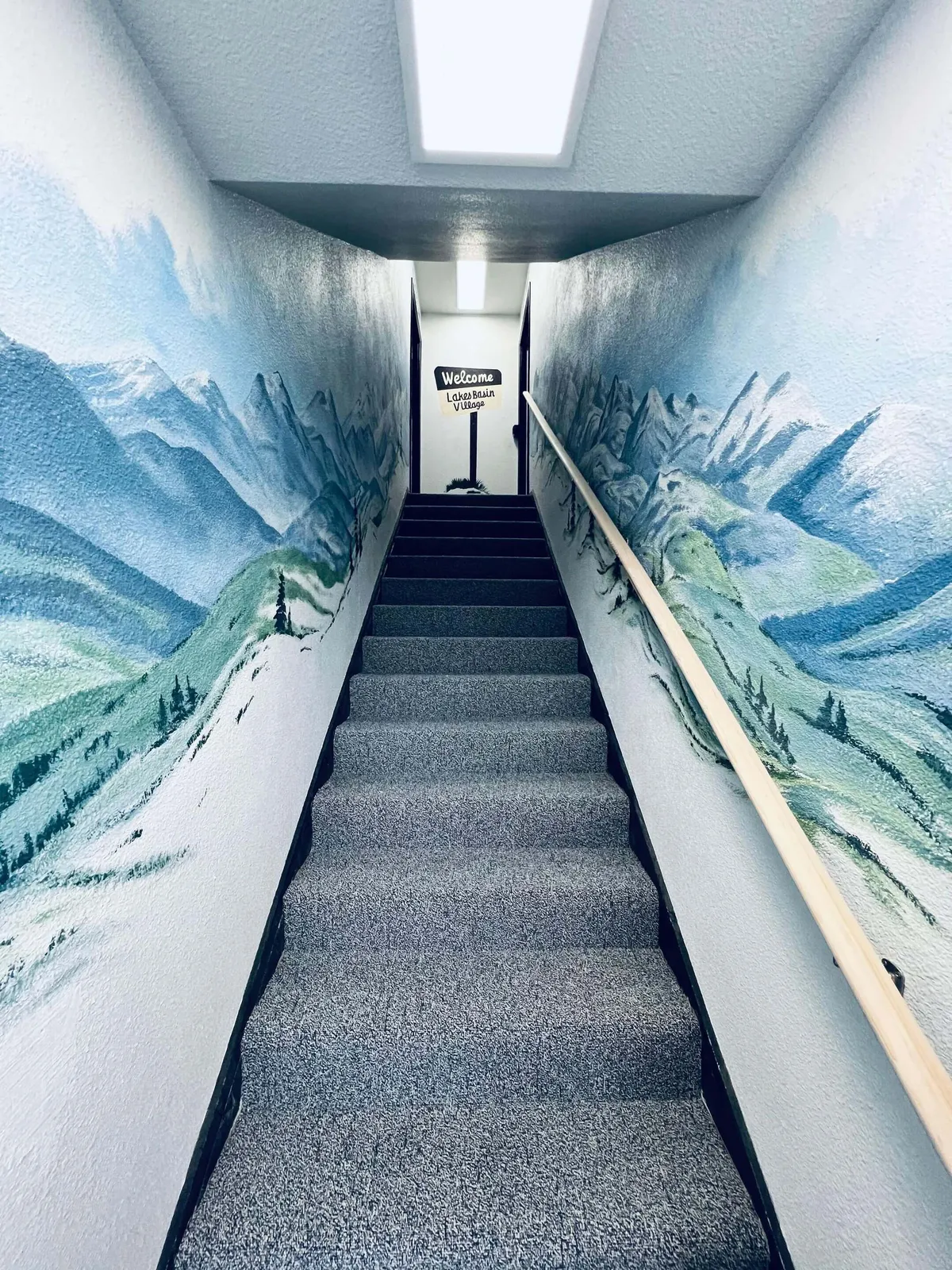 A welcoming entryway featuring a mural of mountains, a prominent staircase, and a friendly welcome sign. The composition immediately evokes a sense of arrival and sets an inviting tone for exploring the property and beyond.