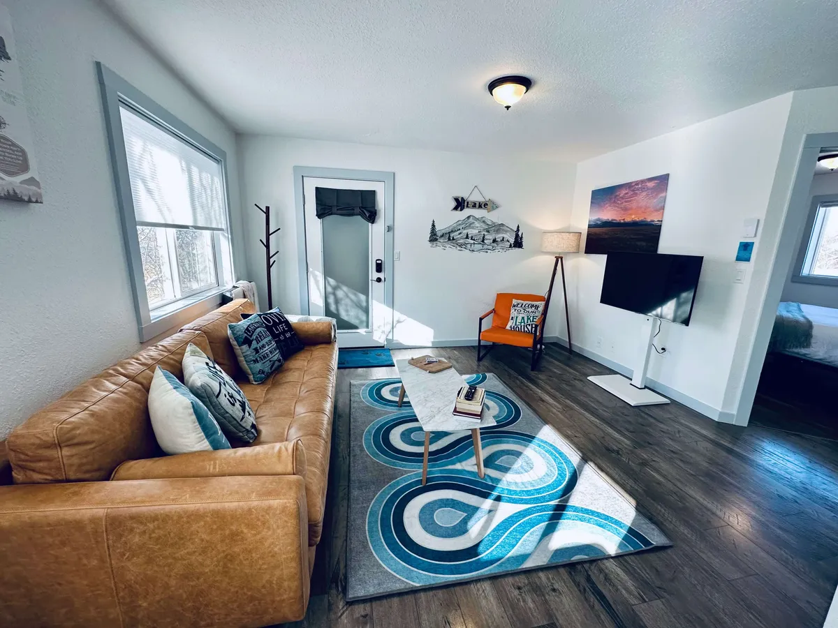 A cozy living room featuring a comfortable leather sofa, a colorful accent chair, decorative wall art, and a TV. Soft morning light streams in, creating an inviting atmosphere for relaxing, reading, socializing, or enjoying a cup of coffee.
